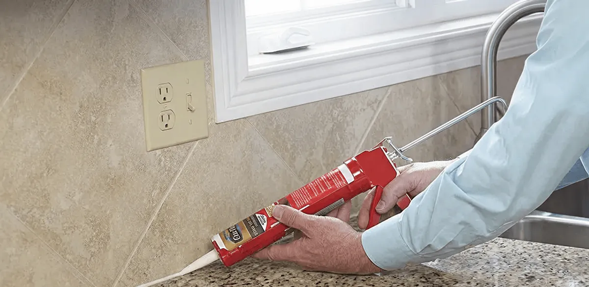 Handyman applying caulk along a kitchen backsplash and countertop seam in Cleveland, OH