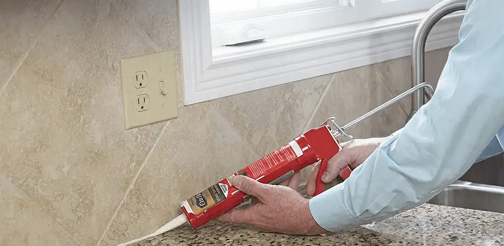 Handyman applying caulk along a kitchen backsplash and countertop seam in Cleveland, OH